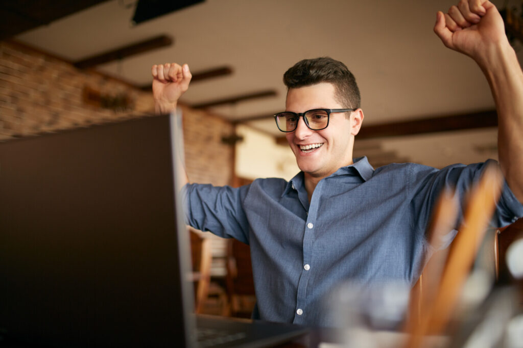 Handsome businessman with laptop having his arms with fists raised, celebrating success. Happy freelancer hipster in glasses finished work on project. Man won a lot of money in lottery prize