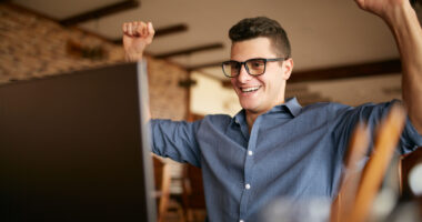 Handsome businessman with laptop having his arms with fists raised, celebrating success. Happy freelancer hipster in glasses finished work on project. Man won a lot of money in lottery prize